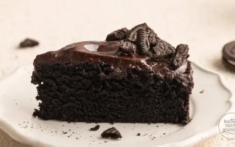 Ein saftiges Stück dunkler Oreo Kuchen mit glänzender Schokoladenglasur und zerbröselten Keksen obendrauf.
