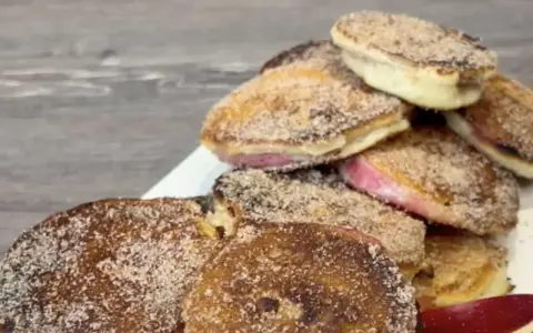 Ein Haufen goldbrauner, mit Zimt und Zucker bestreuter Apfelküchlein, die köstlich aussehen.