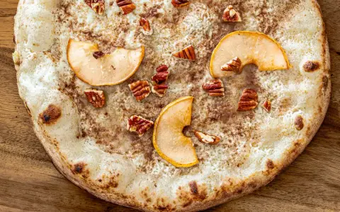 Eine süße Pizza mit dünnem Teig, bestreut mit Zimt, belegt mit Apfelscheiben und Pekannüssen. Ein Genuss wie eine Nutella Pizza!