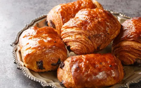 Einige goldbraune, knusprige Pain au Chocolat liegen auf einer silbernen Platte.