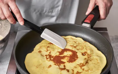 Ein goldbrauner Quark Pfannkuchen wird in einer Pfanne mit einem Spatel gewendet.