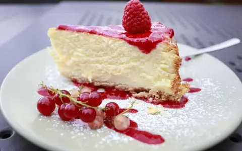 Ein Stück cremiger Käsekuchen mit Himbeersoße und frischen Beeren, bestäubt mit Puderzucker. Ein Genuss für alle Sinne, diese Himbeer Torte.