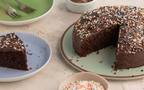 Ein saftiger Nutella Kuchen mit Schokoladenglasur und bunten Streuseln, ein Stück auf einem Teller, bereit zum Genießen.