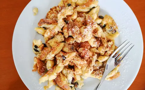 Ein Teller Kaiserschmarrn, bestreut mit Puderzucker und Zimt, wartet auf seine Verkostung. Dieses Kaiserschmarrn Rezept ist ein Klassiker.