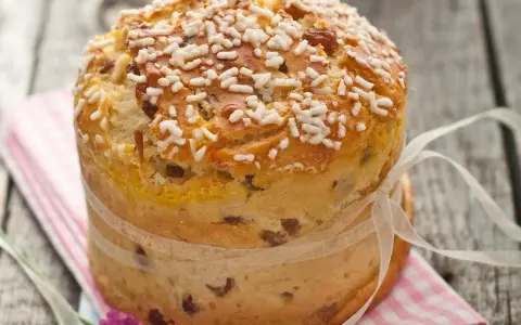 Ein goldbrauner Panettone mit Rosinen und Zuckerkristallen, gebunden mit einem Satinband. Ein köstliches Panettone Rezept zum Nachbacken.