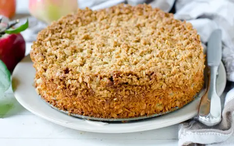 Ein goldbrauner Haferflocken Kuchen mit knuspriger Kruste, daneben Äpfel und ein Messer.