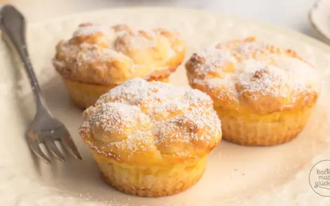 Drei luftige cheesecake muffins, bestäubt mit Puderzucker, warten auf einer Platte auf eine Gabel.