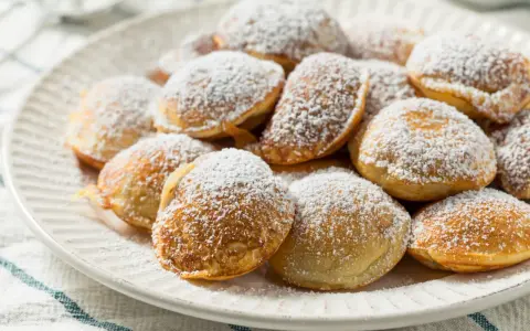 Ein Teller voller goldbrauner Poffertjes, bestäubt mit Puderzucker. Dieses Poffertjes Rezept ist ein Genuss!