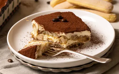 Ein Stück Tiramisu mit Kakaopulver bestäubt, bereit zum Genießen. Dieses klassische Tiramisu Rezept ist ein Genuss.