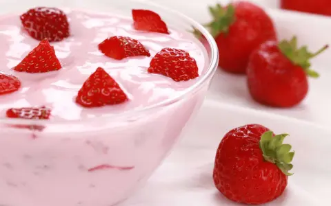 Ein cremiges Erdbeer Dessert in einer Schüssel, garniert mit frischen Erdbeerstücken. Daneben liegen ganze Erdbeeren.