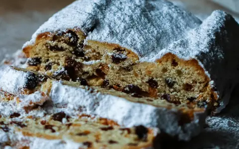 Ein saftiger Stollen, bestäubt mit Puderzucker, zeigt sein Inneres voller Rosinen. Ein köstliches Stollen Rezept zum Nachbacken.