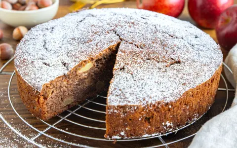 Ein saftiger russischer Apfelkuchen, bestäubt mit Puderzucker, wartet auf seine Genießer. Apfelstücke sind im dunklen Teig sichtbar.