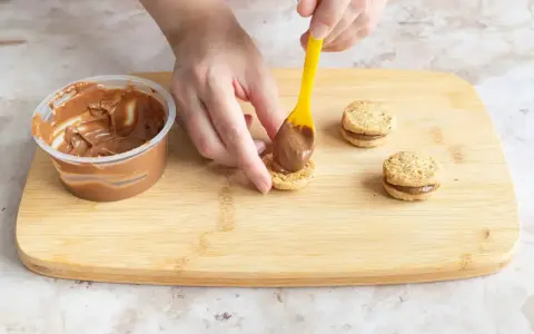 Hände belegen Kekse mit Nutella. Leckere Nutella Kekse entstehen auf dem Holzbrett.