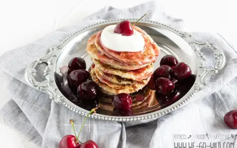 Ein Stapel Bananen Pancakes mit Kirschen und Sahne auf einem Silbertablett, garniert mit frischen Kirschen.