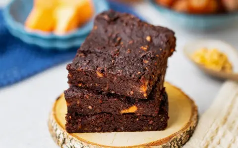 Gestapelte, saftige vegane Brownies mit Nüssen, auf einem Holzscheit.