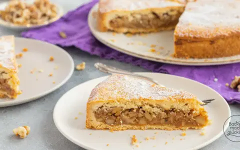 Ein Stück Nusstorte mit Puderzucker bestreut, perfekt für ein leckeres nusstorte rezept. Walnüsse liegen daneben.