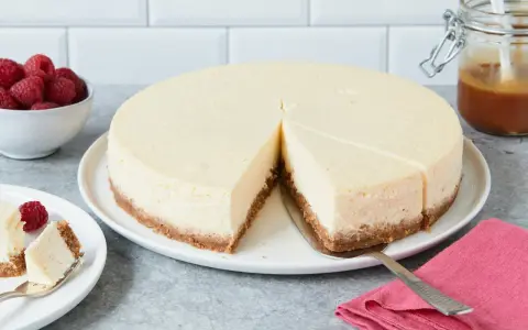 Ein cremiger New York Cheesecake mit knusprigem Boden, garniert mit Himbeeren und Karamell.