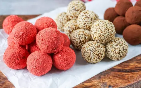 Drei Sorten leckere Energy Balls: rote Erdbeer-Bällchen, mit Sesam umhüllte Kugeln und schokoladige Trüffel.
