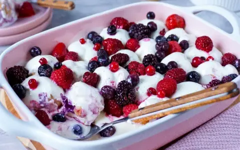 Ein cremiges Windbeutel-Dessert mit frischen Beeren wie Himbeeren, Brombeeren und Blaubeeren, serviert in einer rosa Schale.