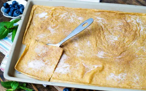 Ein frisch gebackener Ofenpfannkuchen, bestreut mit Zucker und Zimt, bereit zum Servieren. Ein Stück wird mit einem Löffel herausgehoben.