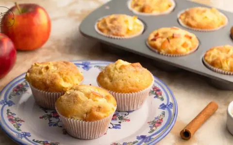 Frisch gebackene Apfelmus Muffins auf einem Teller, daneben Äpfel und Zimt.