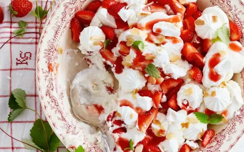Ein köstlicher Eton Mess mit frischen Erdbeeren, Baiser und Sahne, garniert mit Mandelsplittern und Minze.