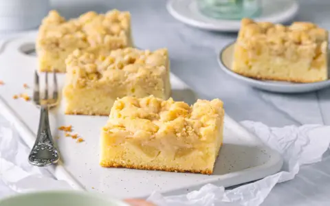 Saftiger Apfelkuchen mit Streuseln, perfekt für eine Kaffeepause. Ein Stück ist schon auf einer kleinen Platte angerichtet.