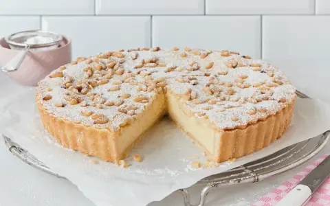 Eine köstliche Torta della Nonna, bestäubt mit Puderzucker und Pinienkernen, wartet darauf, angeschnitten zu werden.