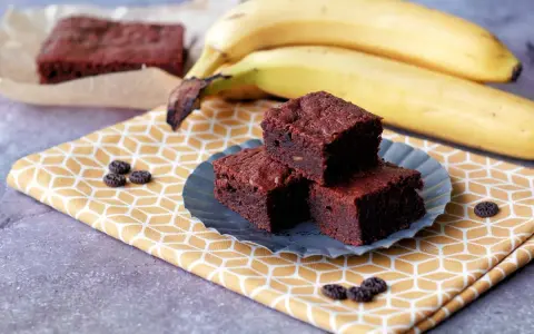 Saftige Bananen Brownies auf einem gelben Tuch, daneben reife Bananen. Ein Genuss!