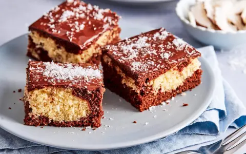 Drei Stücke saftiger Schoko Kokos Kuchen mit Schokoladenglasur und Kokosraspeln auf einem grauen Teller.