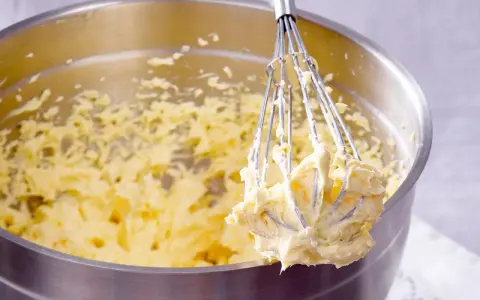 Ein Schneebesen mit cremigem Teig, bereit für ein Buttercreme Rezept.