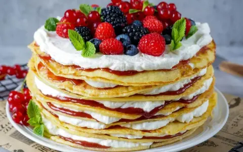 Eine hohe Pfannkuchen Torte mit Sahne und roter Marmelade, gekrönt mit frischen Beeren und Minze.