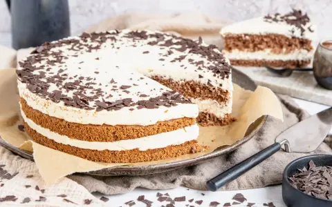 Eine köstliche Cappuccino Torte mit Schokoladenraspeln bestreut, auf einem Teller mit einem angeschnittenen Stück.