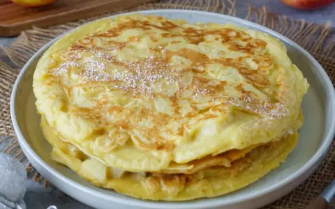 Ein Stapel goldbrauner Apfelpfannkuchen, bestäubt mit Puderzucker. Ein köstliches Apfelpfannkuchen Rezept für jeden Anlass.