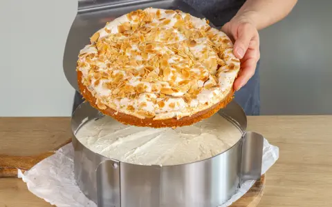 Eine köstliche Stachelbeer Baiser Torte mit Mandel-Topping wird gerade in einen Tortenring gesetzt.