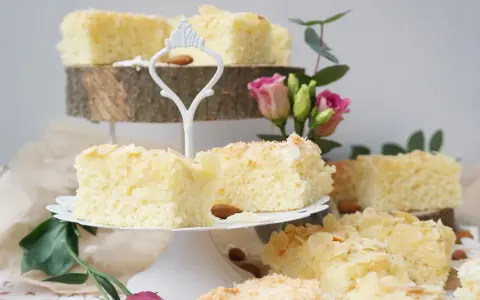 Saftige Buttermilchkuchenstücke mit Mandelsplittern und Kokosraspeln, garniert mit Blumen.