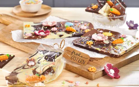 Bruchschokolade selber machen: Bunte Oster-Schokoladentafeln mit Karotten, Blumen und Streuseln, verpackt und mit "Frohe Ostern"-Anhänger.