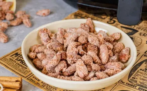 Schüssel voller gebrannter Mandeln, perfekt für ein schnelles gebrannte mandeln rezept. Zimtstangen liegen daneben.