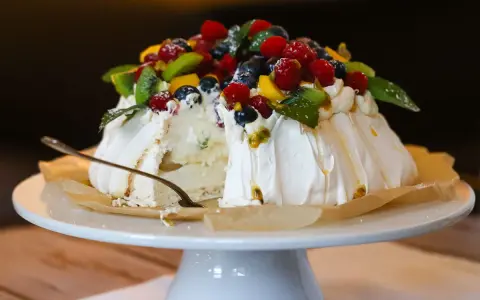 Ein köstliches Pavlova-Rezept mit frischen Beeren, Kiwi und Passionsfrucht. Ein Stück ist bereits angeschnitten.