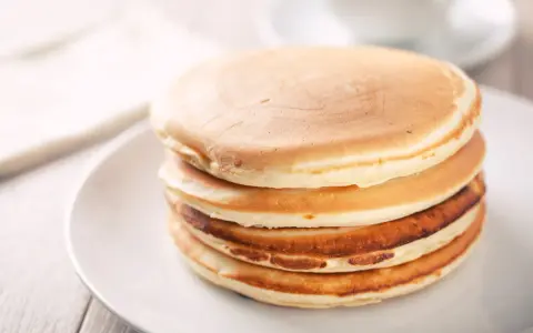 Ein Stapel goldbrauner, glutenfreier Pfannkuchen auf einem weißen Teller, bereit zum Genießen.
