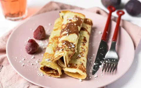 Gefüllte Pfannkuchen ohne Mehl, bestäubt mit Puderzucker, serviert mit Erdbeeren und Feigen.