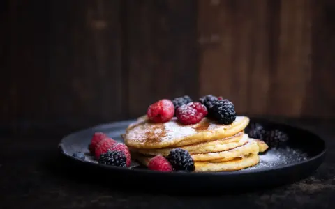 Stapel goldbrauner Pancakes, bestäubt mit Puderzucker und garniert mit frischen Himbeeren und Brombeeren. Ein köstliches Pancakes Rezept für jeden Anlass.