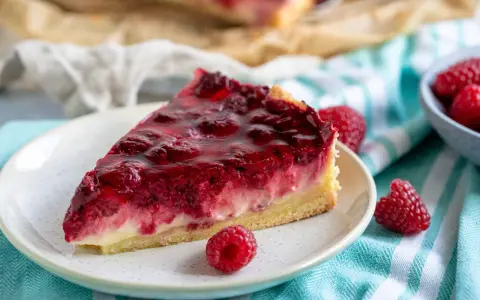 Ein saftiges Stück Himbeer Schmand Kuchen mit frischen Himbeeren und glänzender Glasur auf einem Teller.