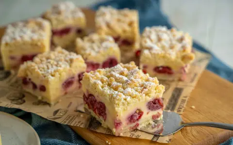 Saftiger Kirschkuchen mit Pudding und Streuseln, bestäubt mit Puderzucker. Ein Stück wird gerade serviert.