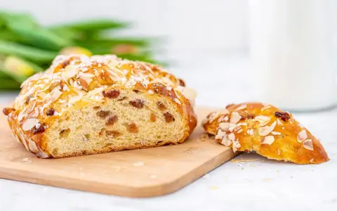 Ein goldbraunes Osterbrot mit Mandelsplittern und Rosinen, perfekt für Ihr Osterbrot Rezept. Daneben ein Stück des süßen Gebäcks.