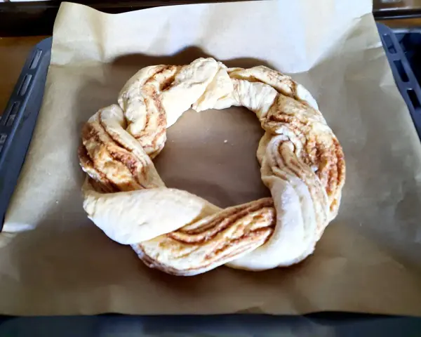 Ein geflochtener Teigring mit Zimtfüllung liegt auf Backpapier. Perfekt für das Osterkranz backen.
