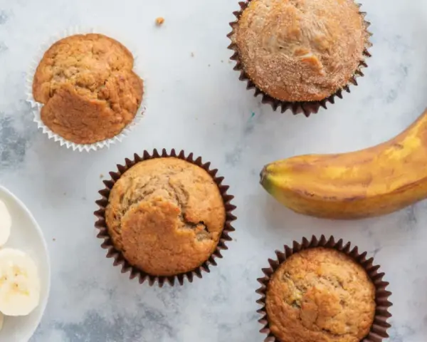 Leckere Bananen Muffins, frisch gebacken, mit einer reifen Banane und Bananenscheiben daneben.