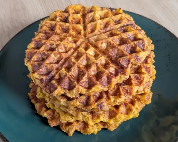 Ein Stapel goldbrauner Haferflocken Waffeln auf einem dunklen Teller. Sie sehen knusprig und lecker aus, perfekt für ein gesundes Frühstück.