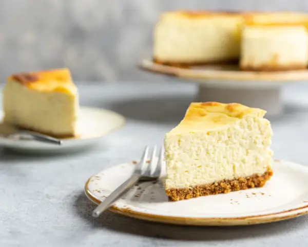Ein cremiger Kuchen mit Mascarpone, auf einem Teller mit Gabel, daneben ein weiteres Stück und ein ganzer Kuchen.