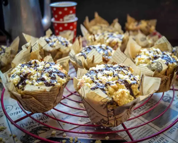 Saftige Nutella Muffins mit Streuseln und Schokoglasur, verpackt in Zeitungspapier-Förmchen, auf einem roten Gitter.